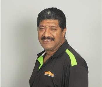 Male employee with black hair in front of tan background